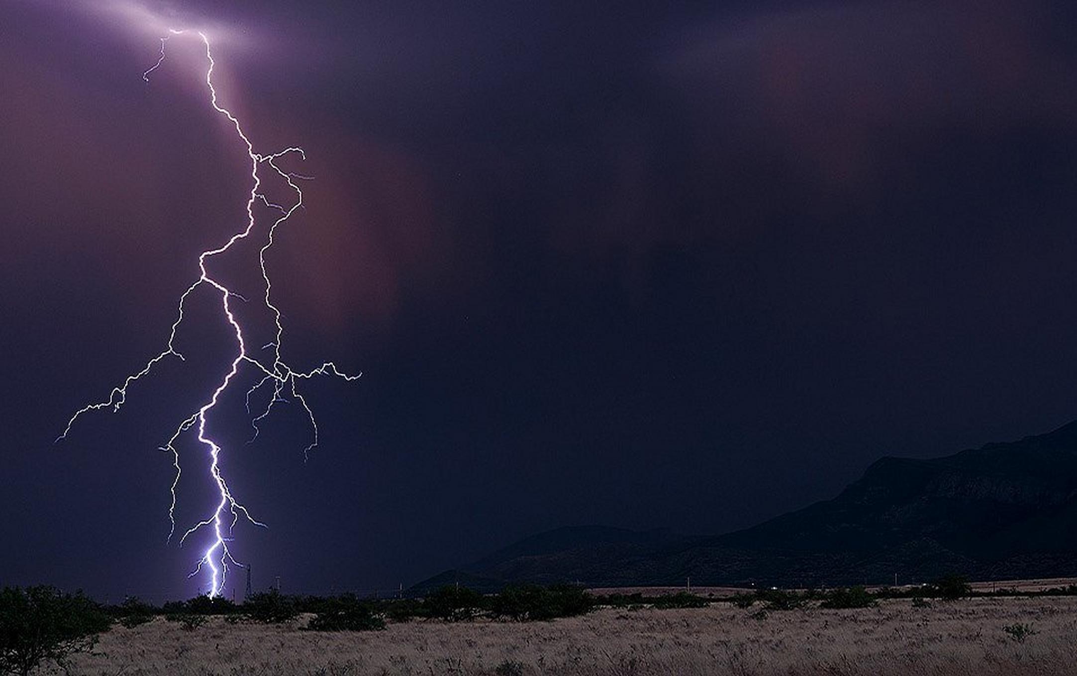 A big desert landscape is framed with a distant mountain range in the background. A single snake-like lightning bolt with multiple tentacles strikes the sparse landscape.