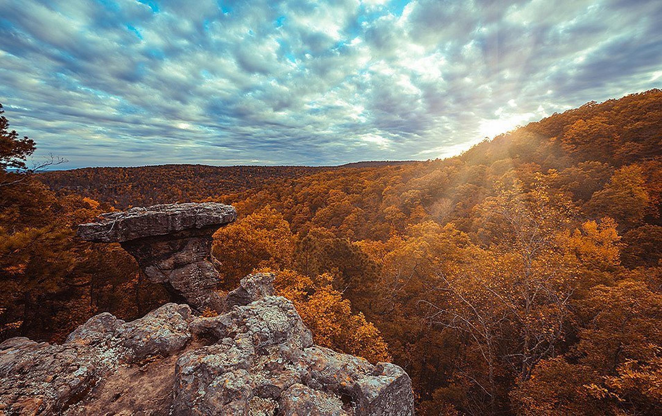 A prominent flat-topped outcrop rises above a hardwood forest with orange foliage.