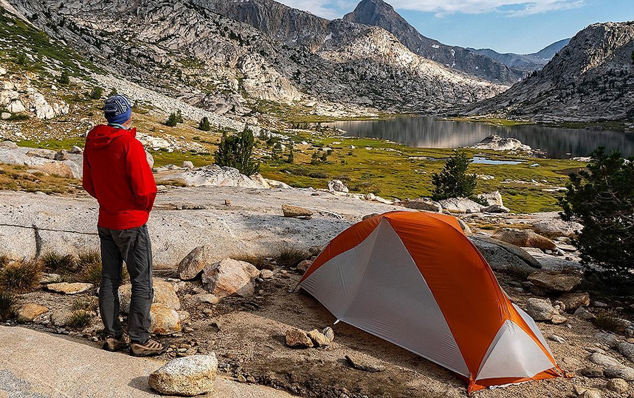 A solo camper has pitched a small tent by an alpine lake.