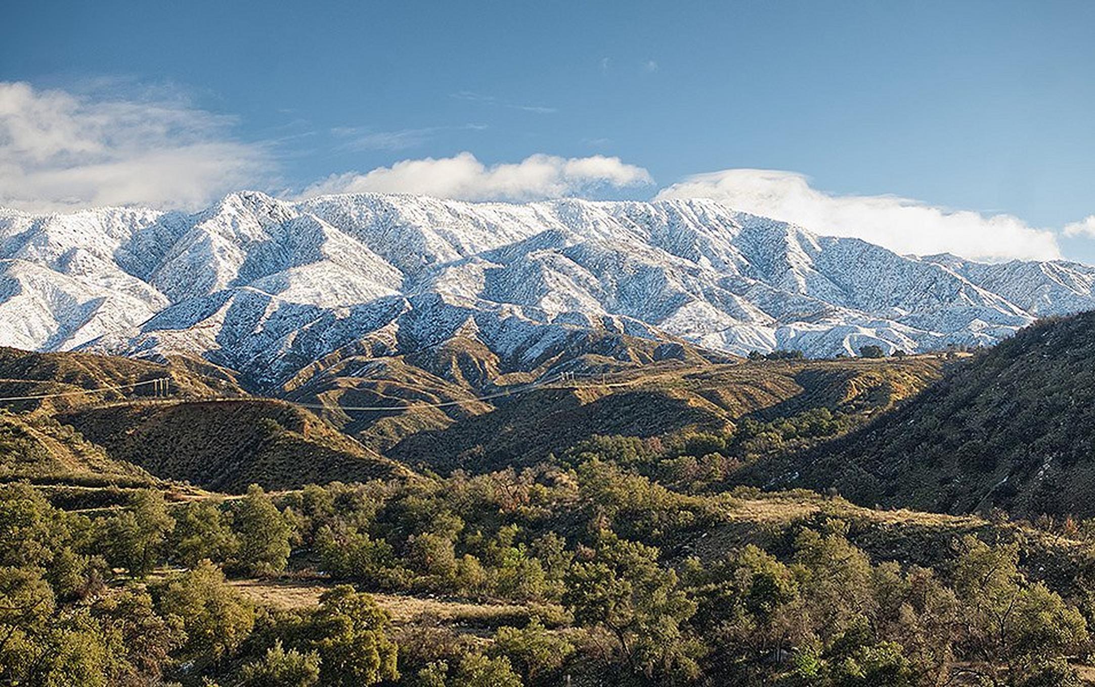 Snow-covered mountains give way to greener foothills and tree-covered valleys.