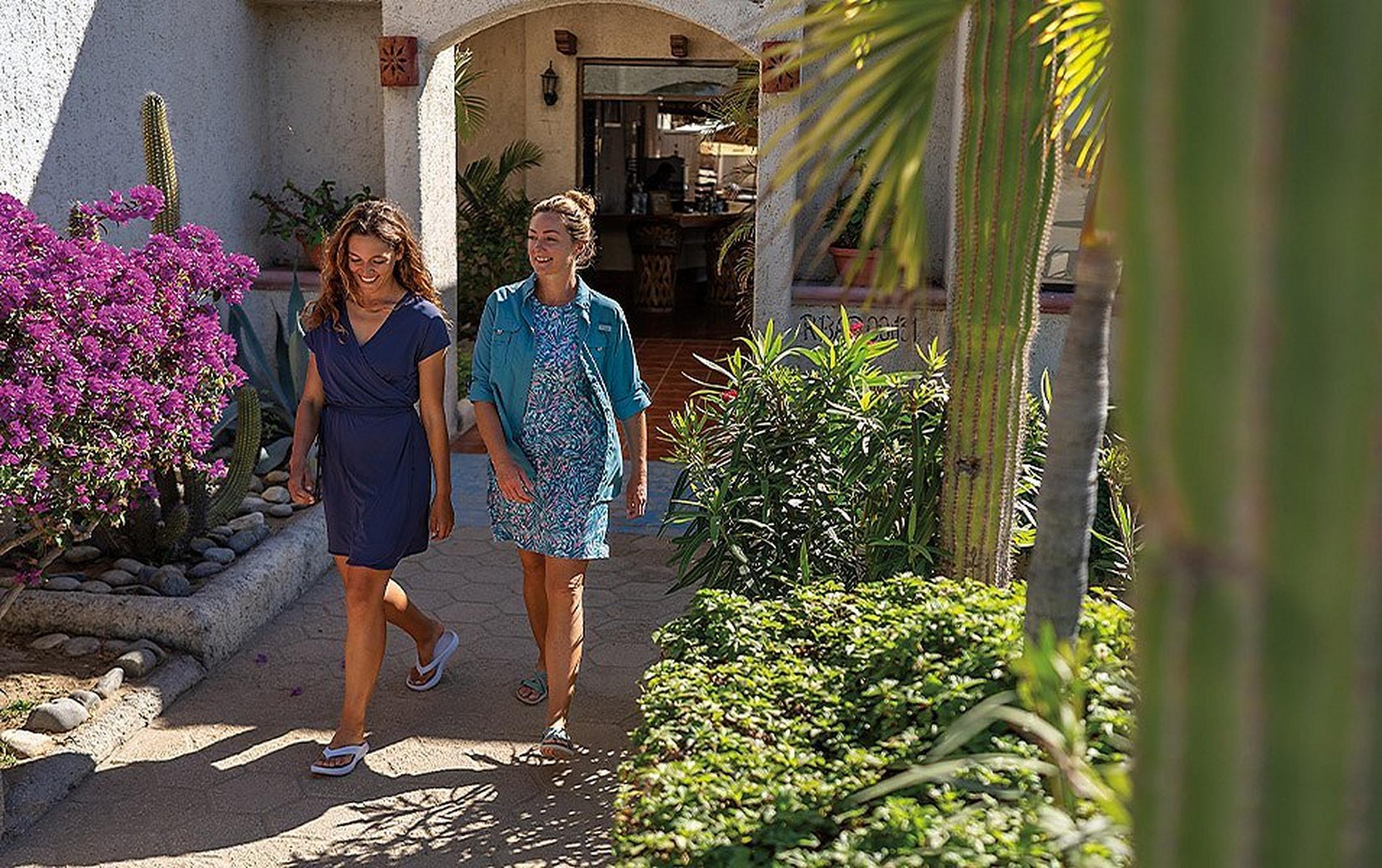 Two people laugh as they walk out onto a sunny courtyard.