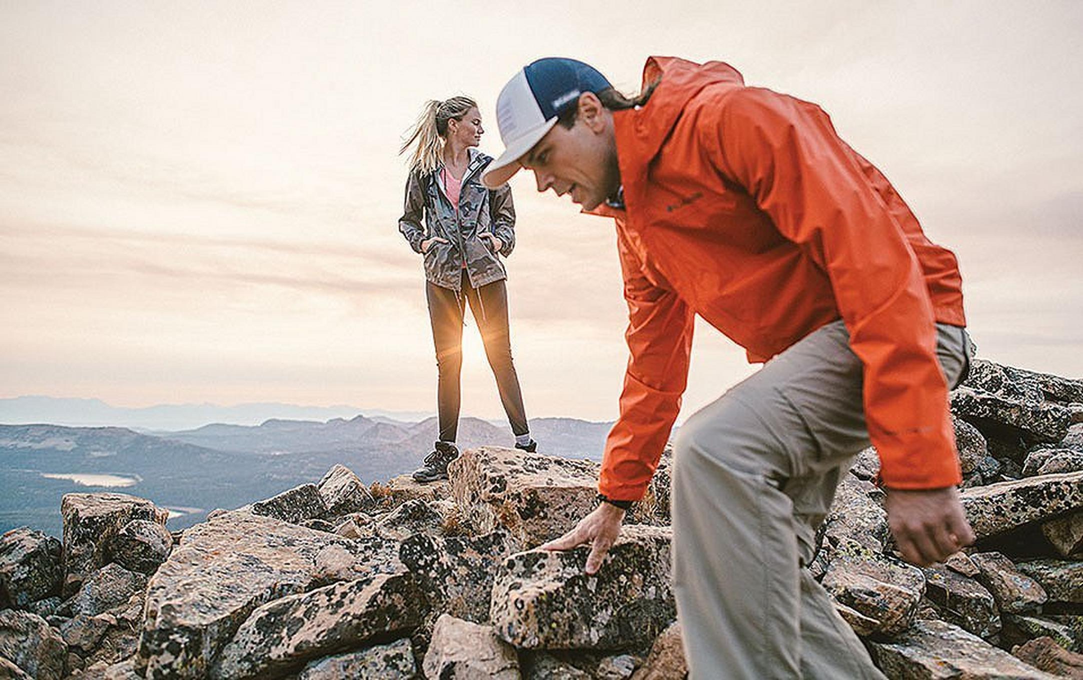 Man and woman walking on the top of mountain at sunset.