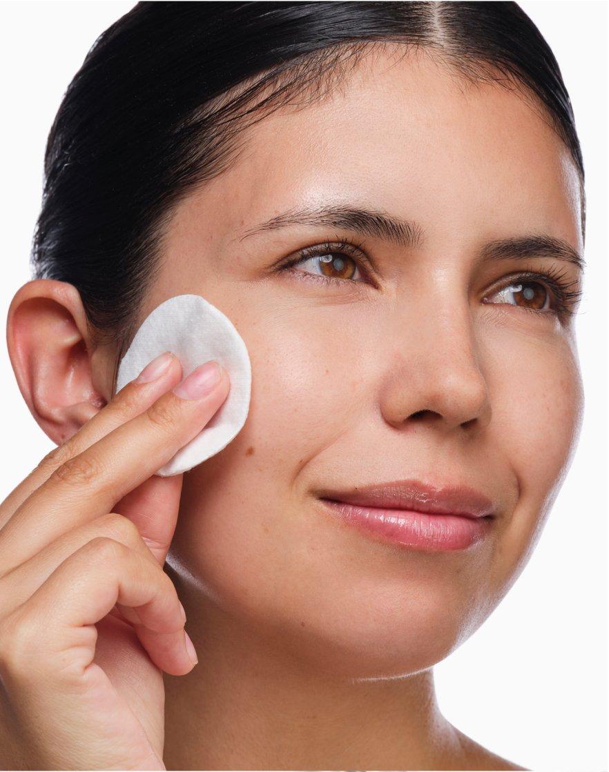 Person applying serum on face with a cotton round.