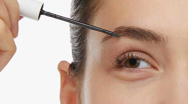 Close-up of a hand precisely applying The Ordinary Multi-Peptide Lash and Brow Serum to groom and nourish eyebrows.