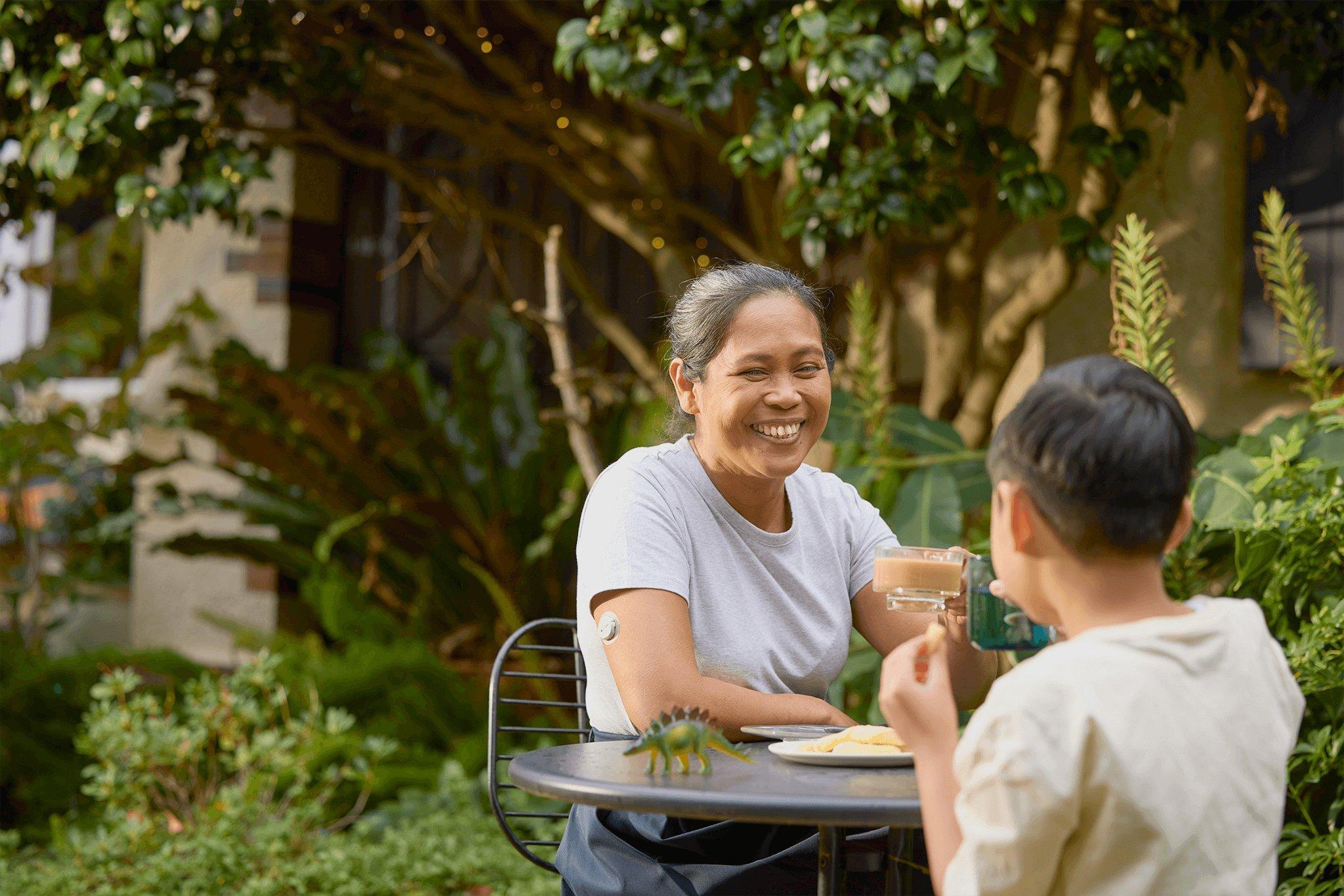 Woman wearing Dexcom ONE+ CGM sensor and having lunch outdoors with her son.