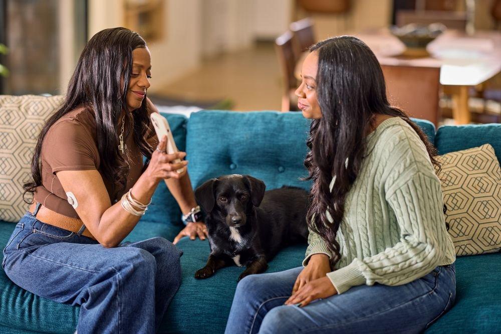 2 Women on a couch with a dog looking at a phone