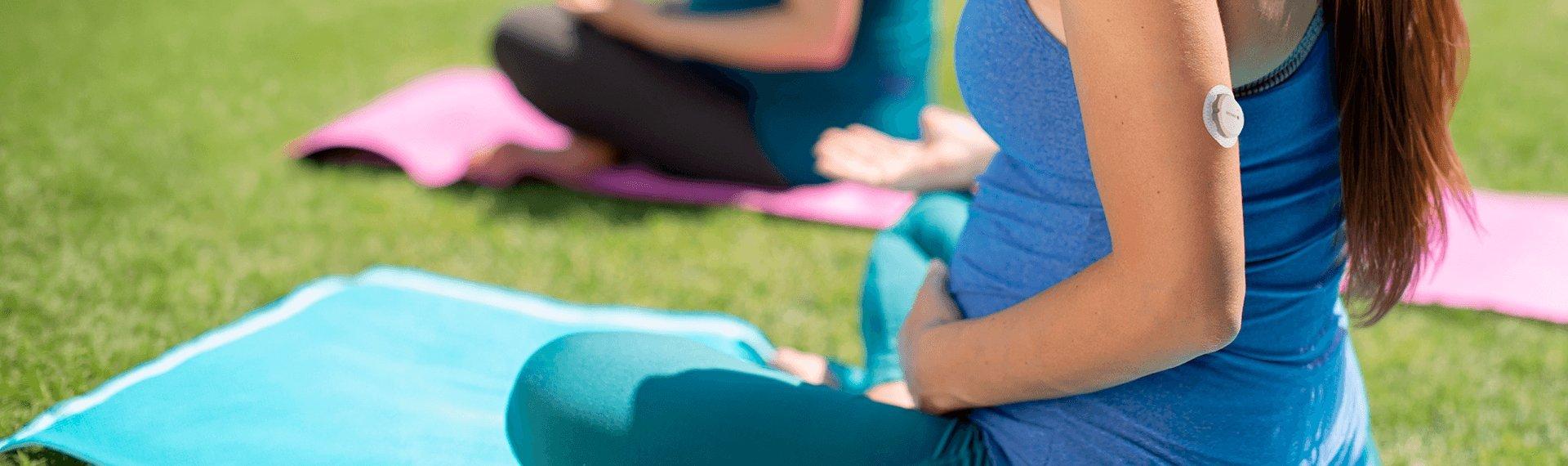 Pregnant woman wearing a Dexcom G7 CGM on the back of her arm and doing yoga outside