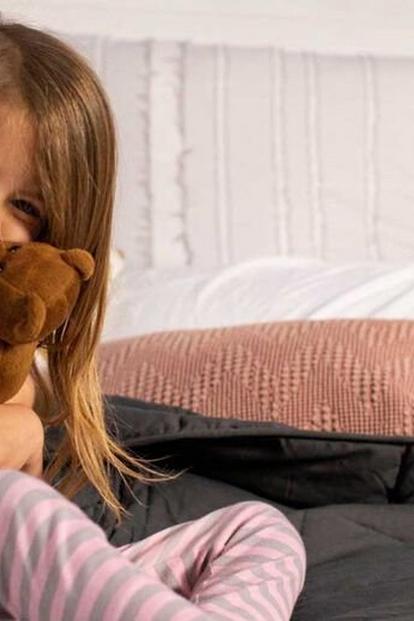 Μικρό κορίτσι αγκαλιάζει μια καφέ αρκούδα και φοράει μια συσκευή συνεχούς παρακολούθησης γλυκόζης Dexcom στο πίσω μέρος του δεξιού της χεριού