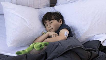 Poiss magab voodis ja kaisutab rohelist pehmet mänguasja