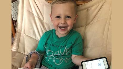 Mažas berniukas žaliais marškinėliais šypsosi ir laiko išmanųjį telefoną