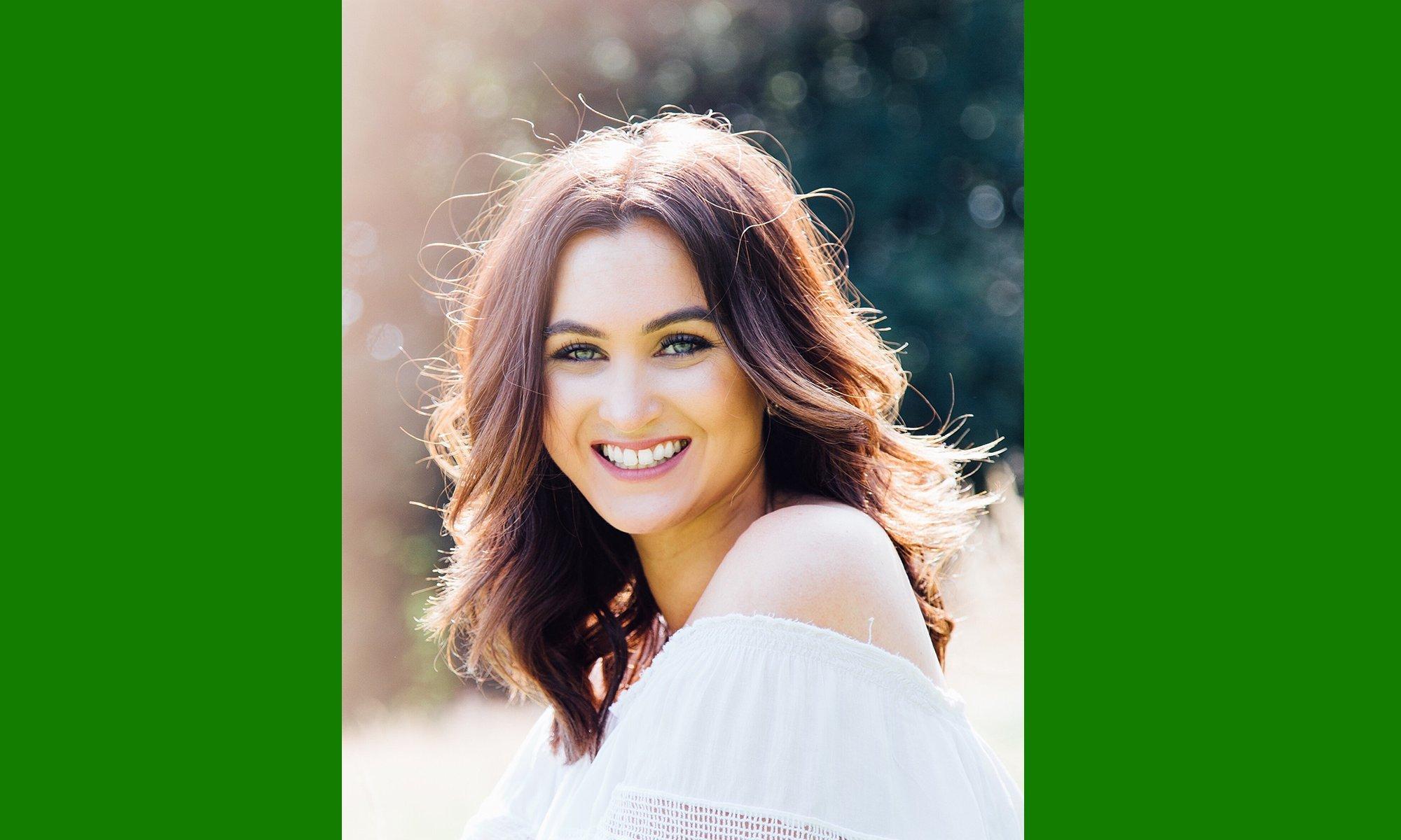 red-headed girl with blue eyes smiling in the camera while sitting in front of a forest