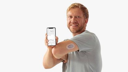 Човек показва приложение Dexcom на смартфон и едно устройство Dexcom на гърба на ръката си