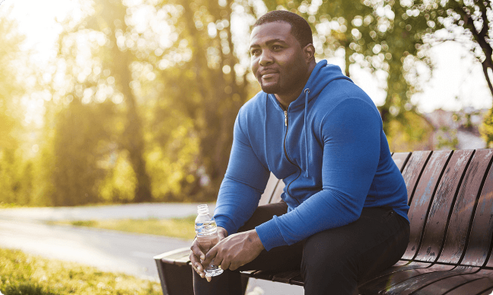 Man sitting on a bench outside drinking water