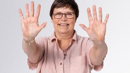 Sieviete paceļ roku pret kameru, lai nerādītu pirkstu dūrienus