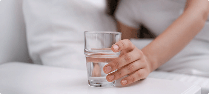 hand holding a cup of water on a nightstand