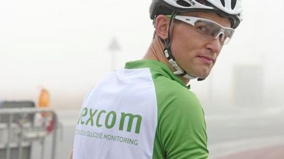 Αρσενικό ποδηλασία φορώντας κράνος και επώνυμα ρούχα της Dexcom