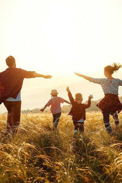 Mlada družina teče po polju z odprtimi rokami in zahajajočim soncem v ozadju