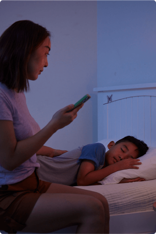 woman checking on son sleeping while holding a smart device