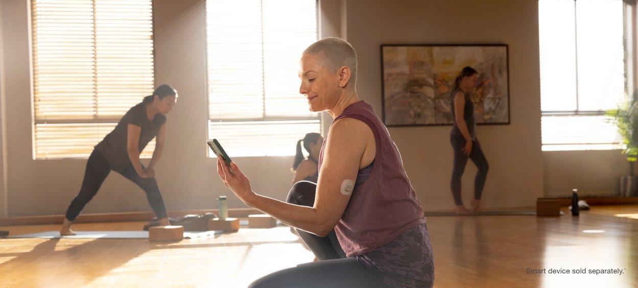 Woman looking at phone while wearing the Dexcom G7 sensor - Smart device sold separately*