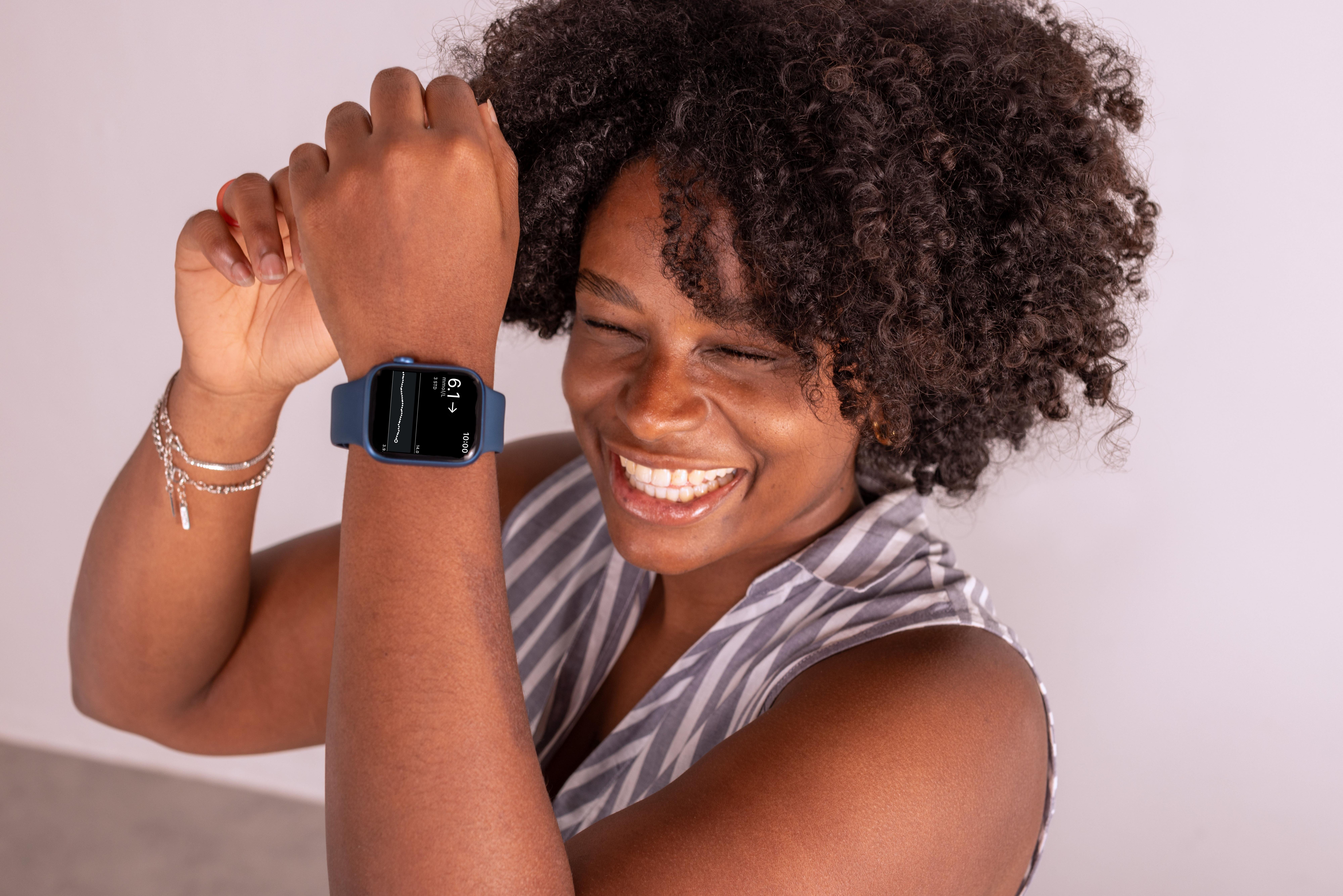 Woman laughing while wearing an apple watch that is showing her glucose levels transmitted from dexcom g7