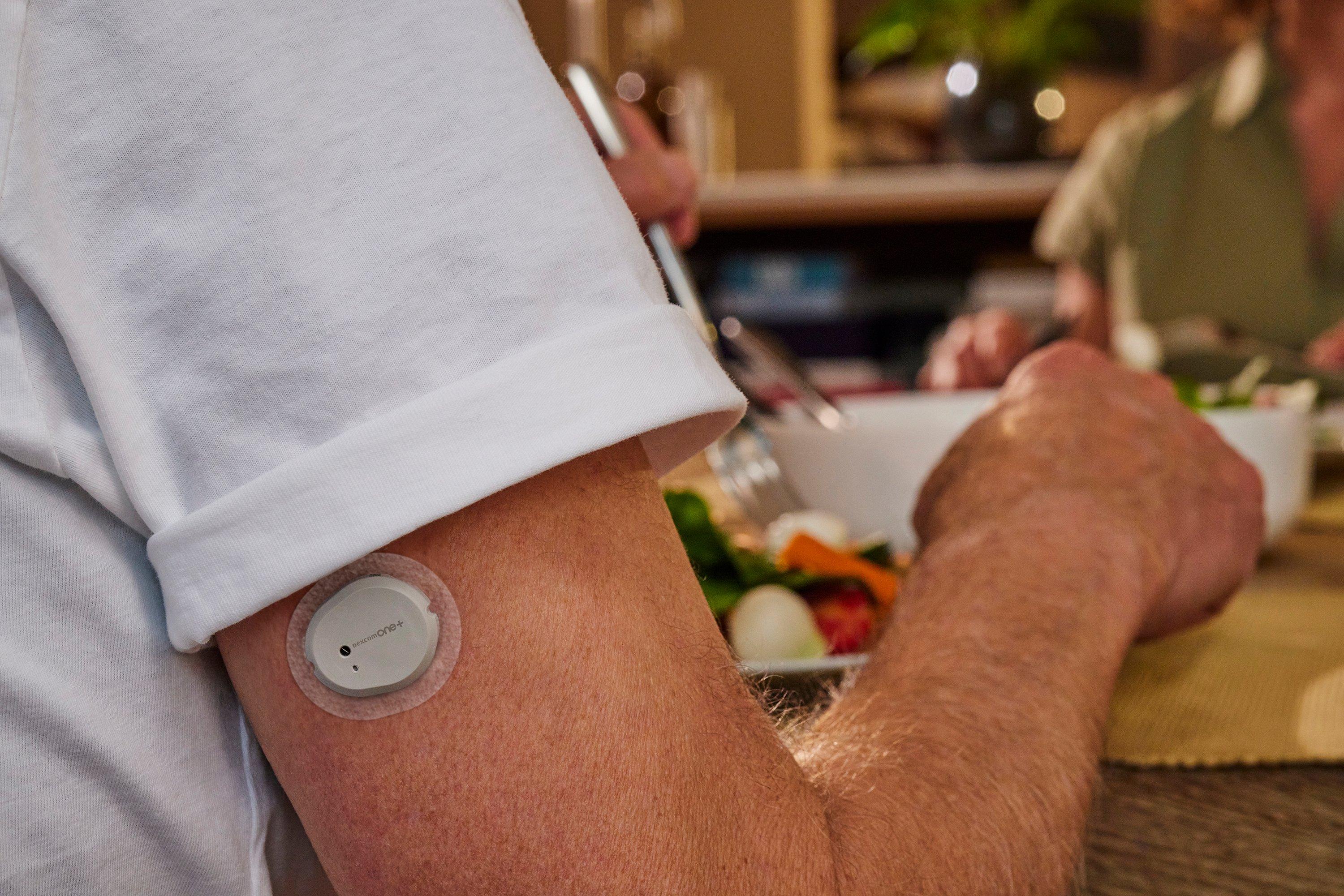رجل يجلس على طاولة ويحمل جهاز Dexcom One+ على ذراعه