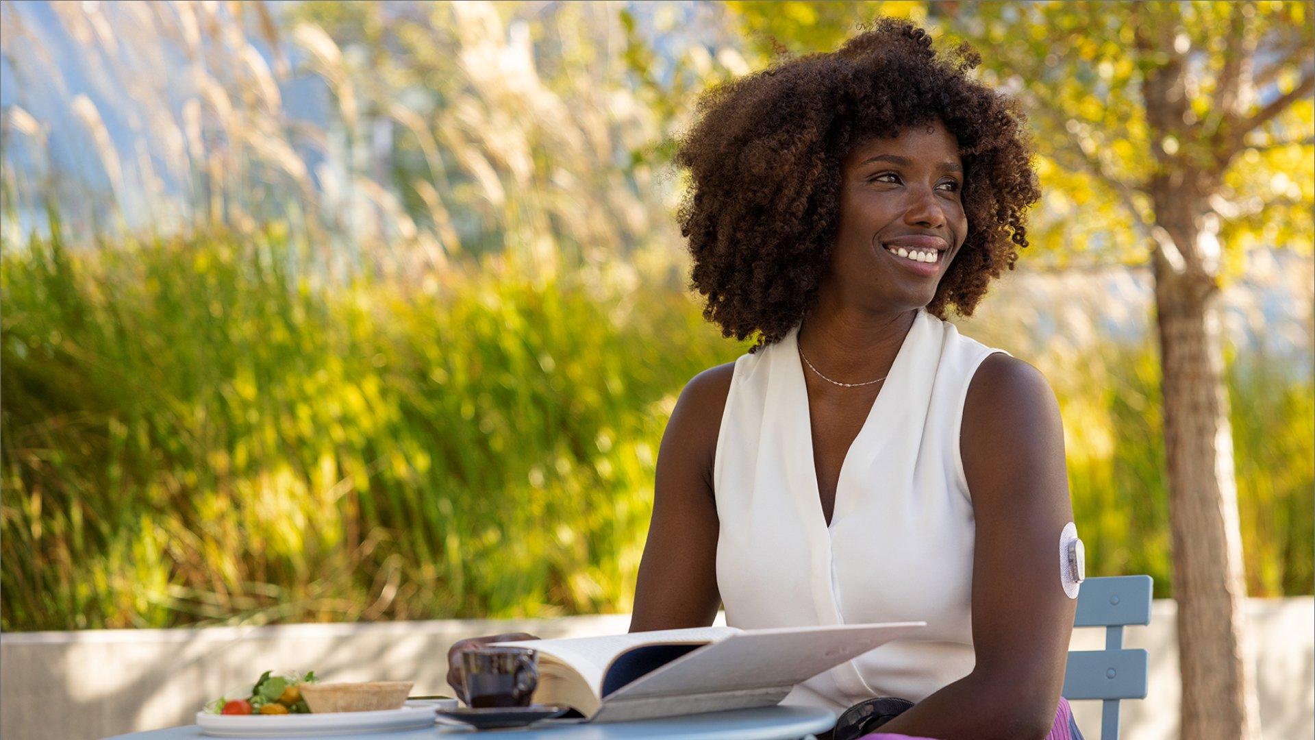 woman with white top sitting at cafe table with book