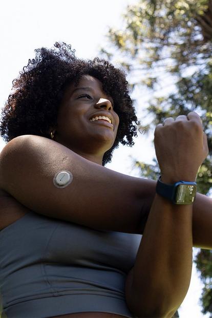 Women in park stretching her arm with a Dexcom G7 sensor on her upper arm and an Apple Watch on her wrist