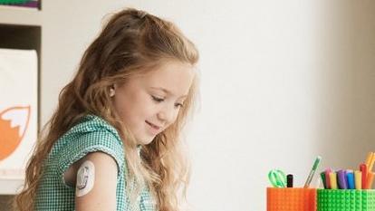 Young school girl with paediatric diabetes who wears a Dexcom sensor on her arm while doing arts and crafts