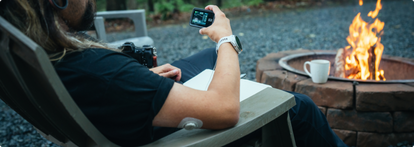Man checking Tandem t:slim wearing Dexcom G7 sitting at campfire