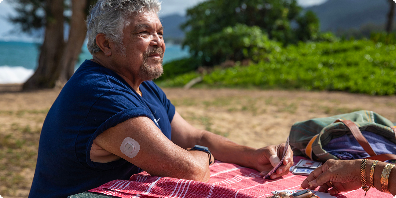 Man smiling sitting at picnic table playing cards with Dexcomg G7 back of arm