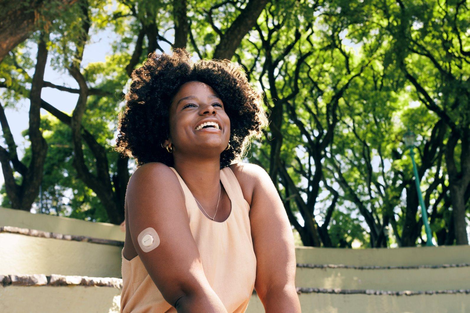 woman smiling outside wearing dexcom