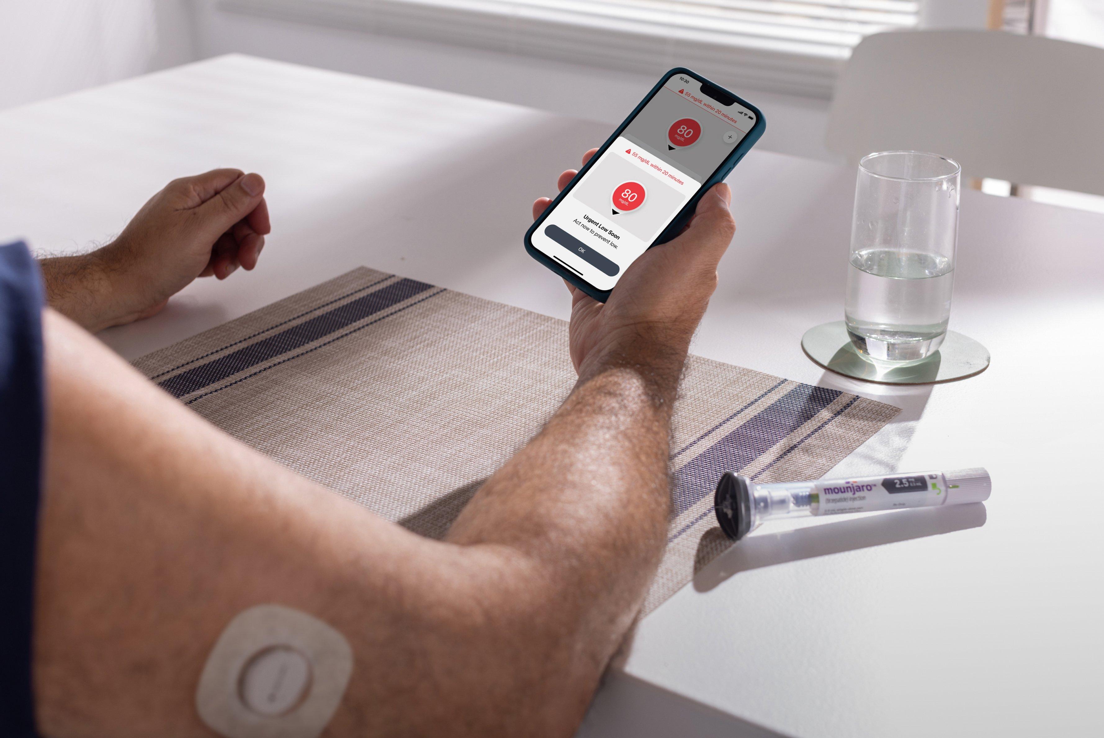 Person looking at urgent low alert on thier smaartphone, wearing the dexcom CGM sensor