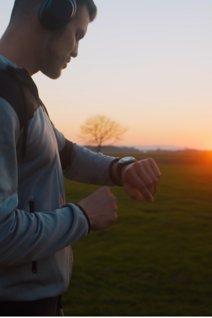 Mann trägt Kopfhörer und schaut bei Sonnenuntergang auf seine Uhr