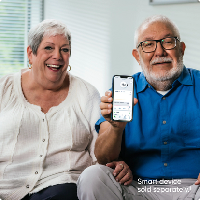 two people sitting on couch smiling holding a smartphone with the dexcom app screen showing