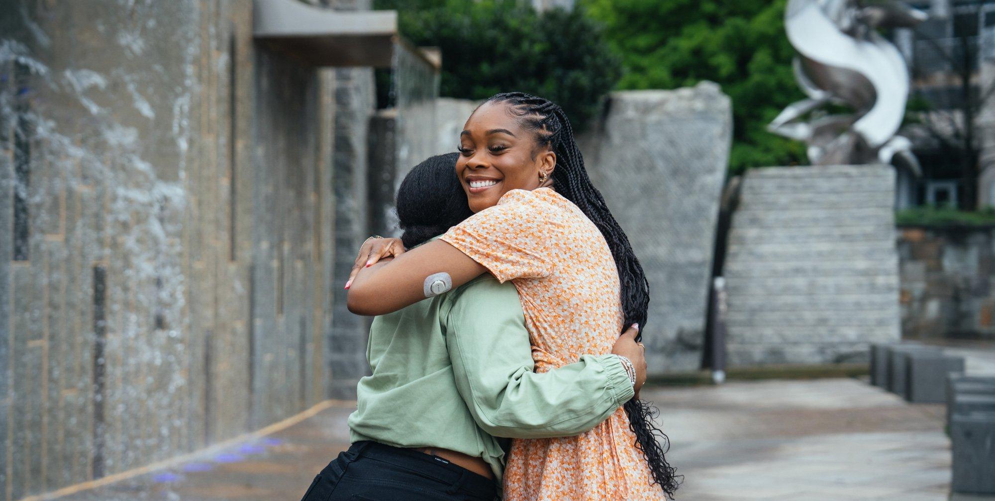 Women hugging smiling wearing Dexcom G7 sensor back of arm