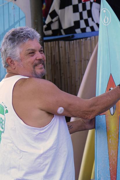 man smiling looking at surfboards wearing dexcom g7 sensor