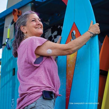 woman holding surfboard smiling with sensor on arm