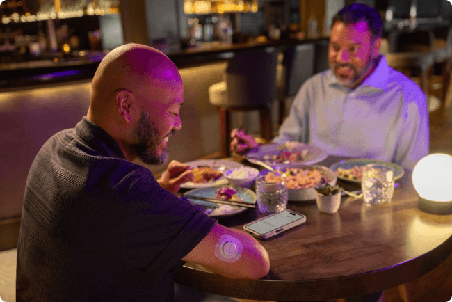 Chris out having dinner with a friend while wearing Dexcom sensor and looking at his phone on the table