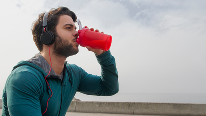 Man outside drinking a creatine drink while listening to music