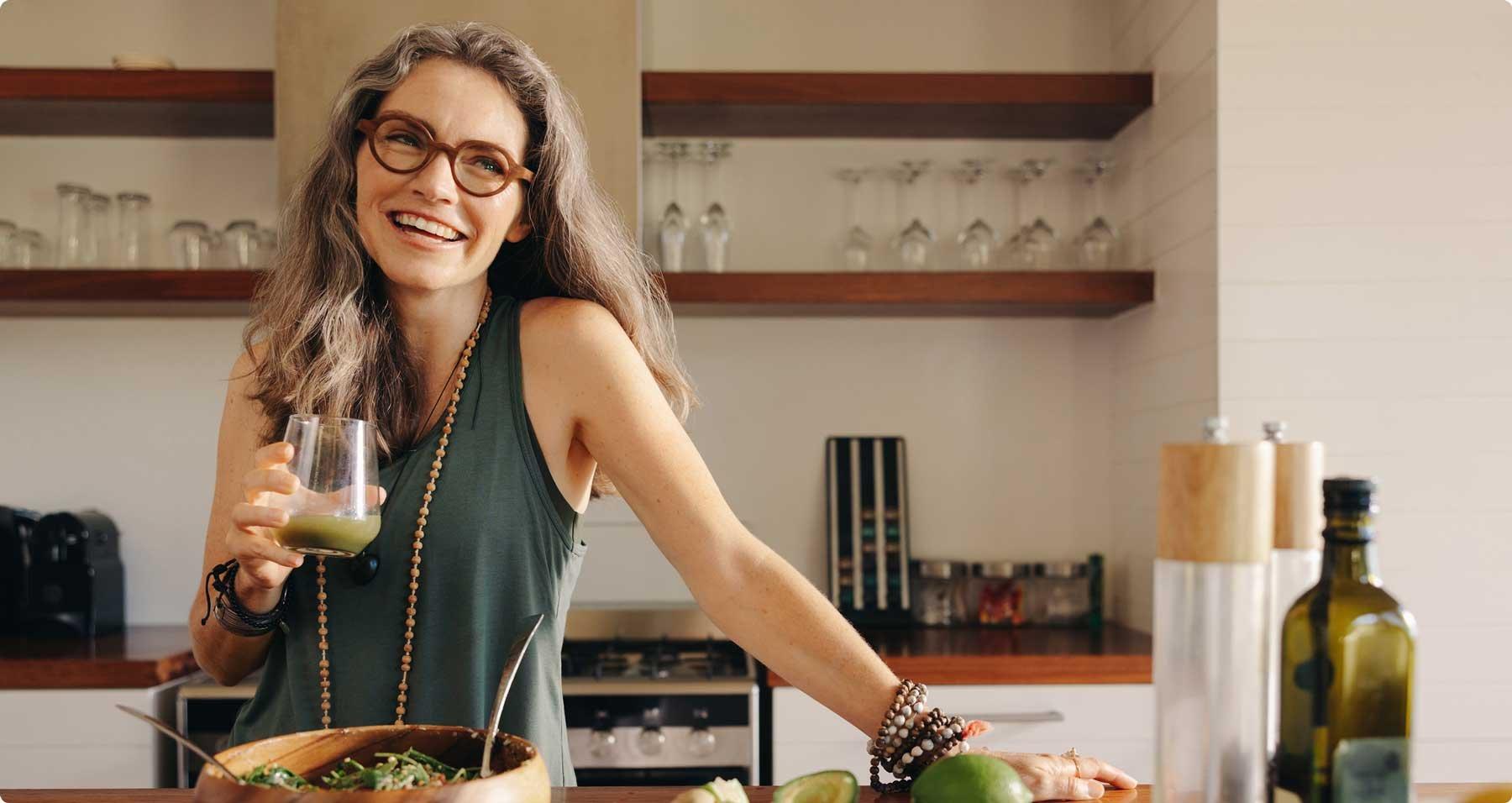 Woman in her kitchen drinking a drink while preparing a salad