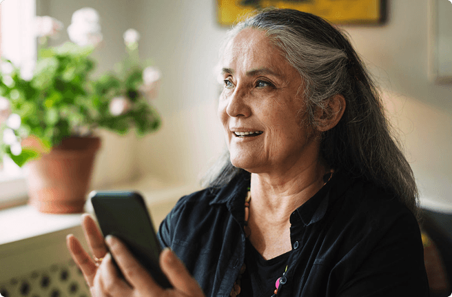 Woman with partially gray hair holding her phone and looking to the left
