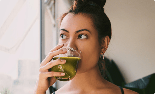 Woman drinking green drink and looking out a window