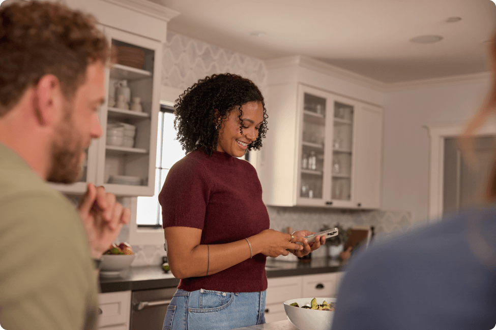 Woman wearing Stelo sensor taking picture of her food with friends in her kitchen