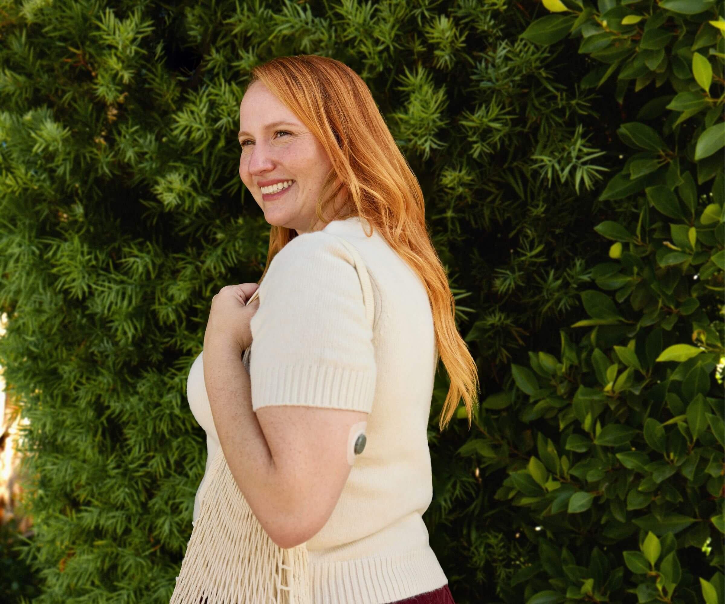 Woman wearing Stelo sensor smiling in front of greenery