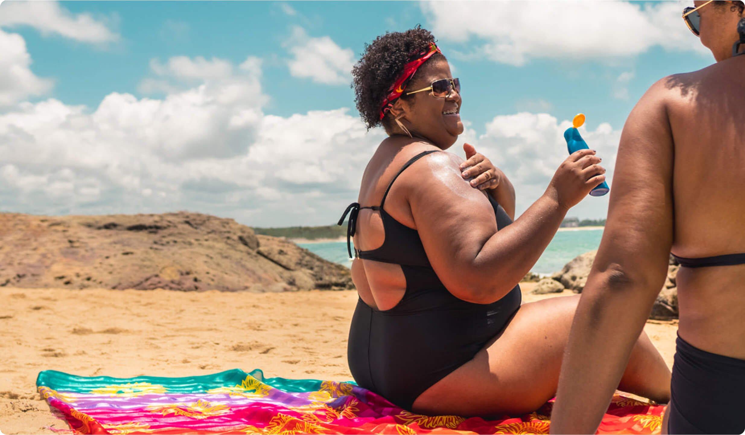 Two women sitting on a towel at the beach applying sunscreen