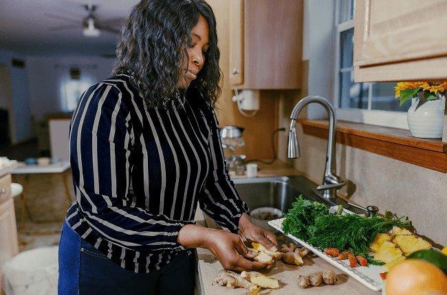 Woman peeling ginger in her kitchen over a cutting board next to a sink