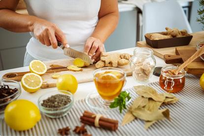 Woman cutting ginger on a cutting board in her kitchen surrounded by ingredients