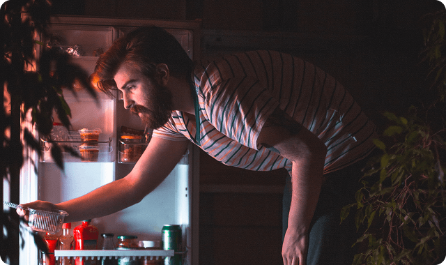 Man bending over and looking into the fridge at night