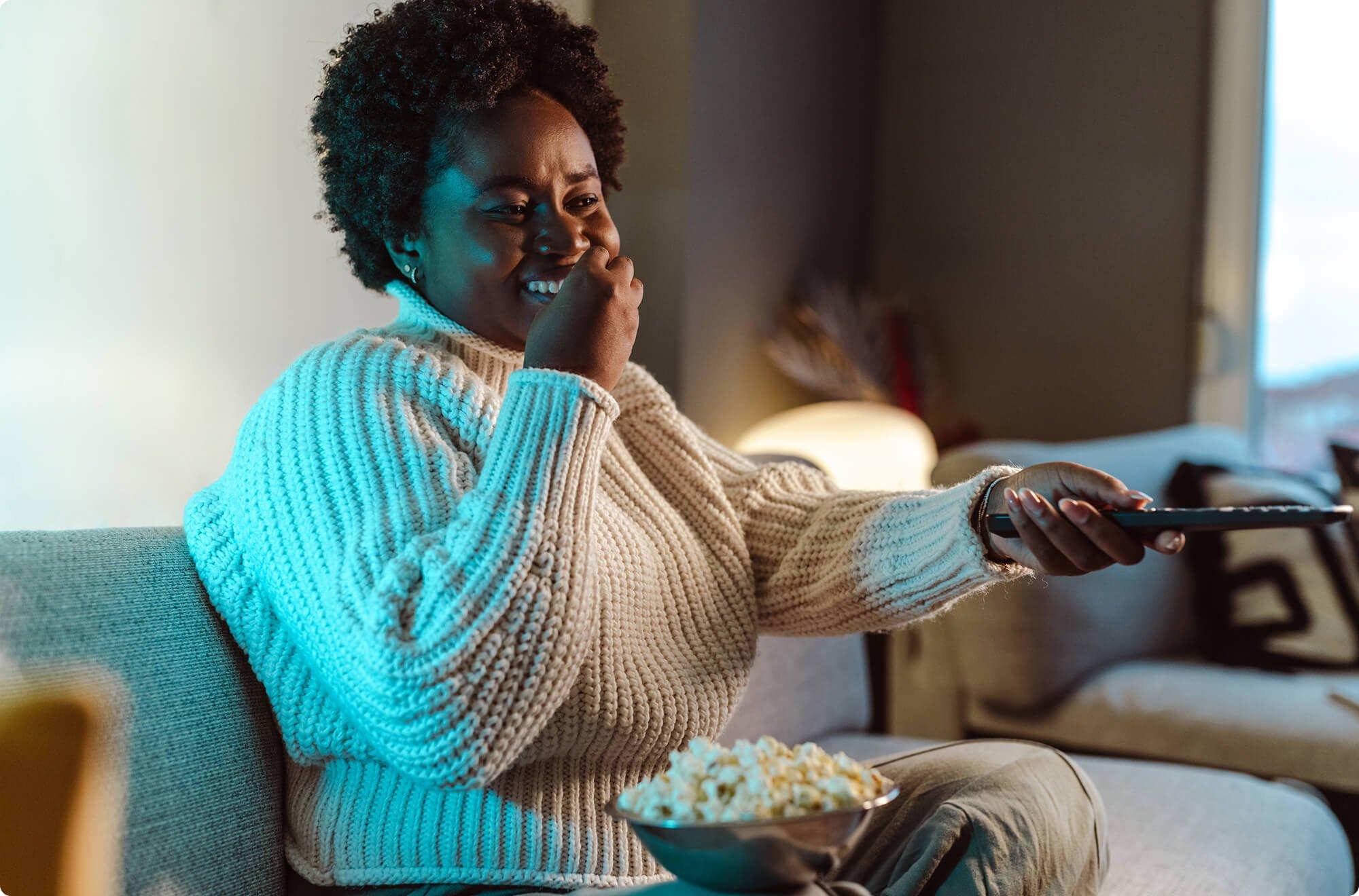 Woman sitting on her couch eating popcorn while watching tv