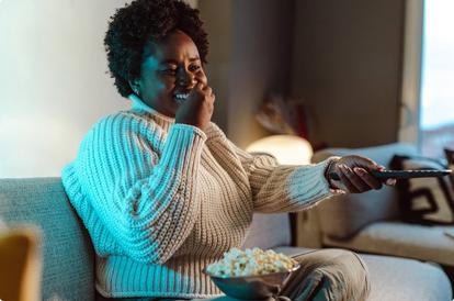 Woman sitting on her couch eating popcorn while watching tv